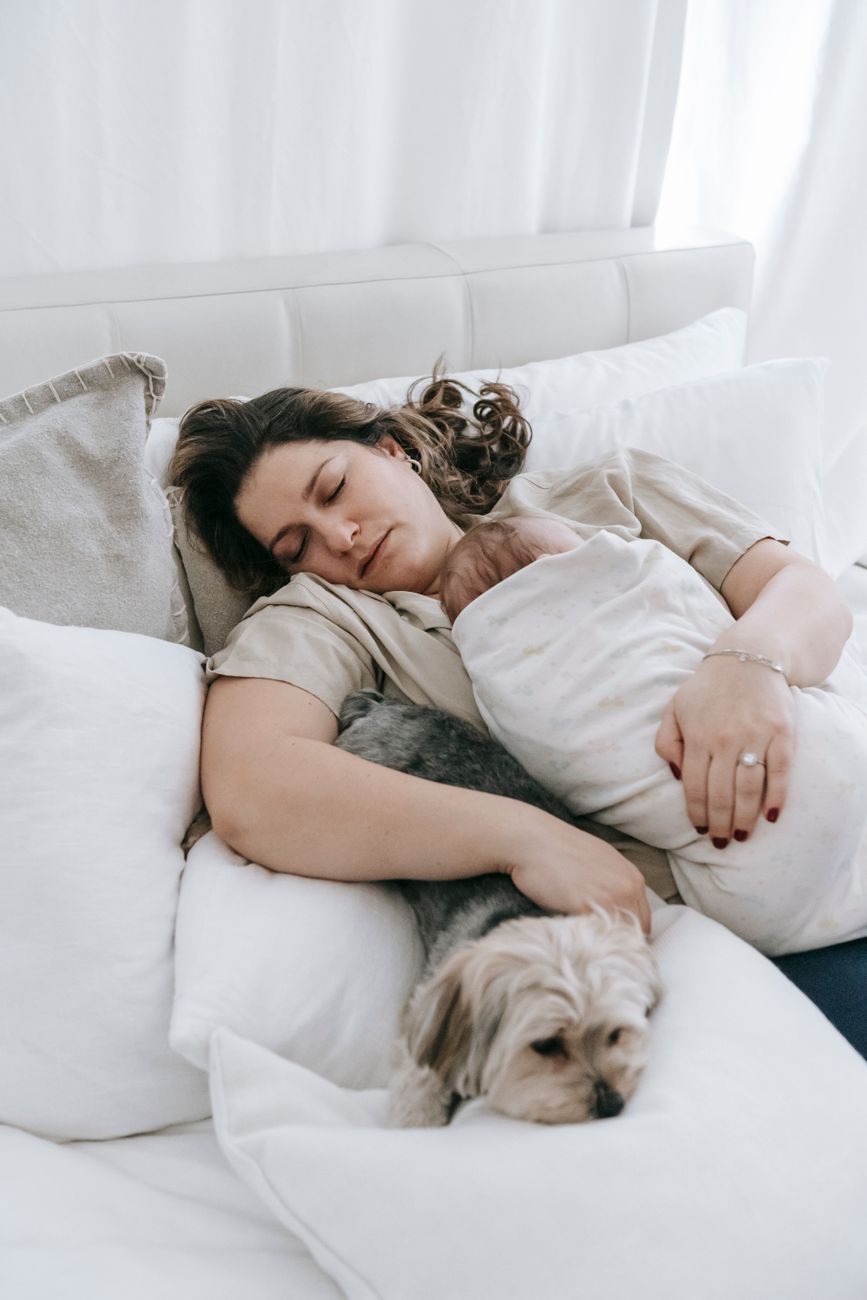 mother with baby sleeping on bed with dog